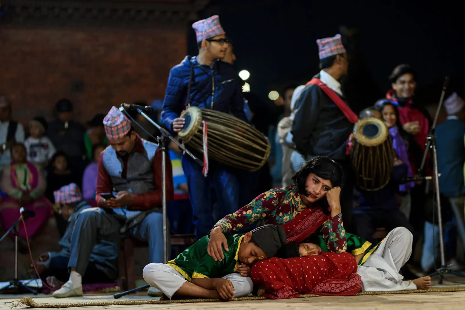Musicians with drums play beside performers acting out a scene on the stage